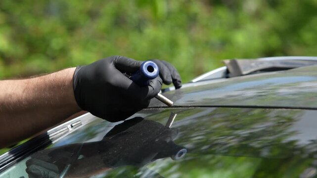 4K video of cutting windshield urethane with a wire removal tool. Mechanic using a wire grip tool to cut old polyurethane adhesive and remove a broken car windshield