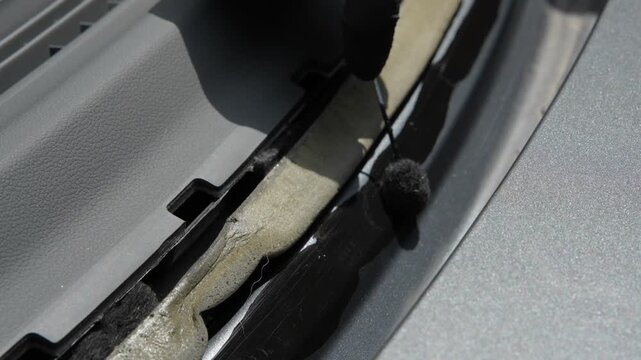 4K video of applying black primer to the lower windshield pinchweld. Mechanic using a wool dauber to apply urethane primer to the vehicle frame near the dashboard cowl