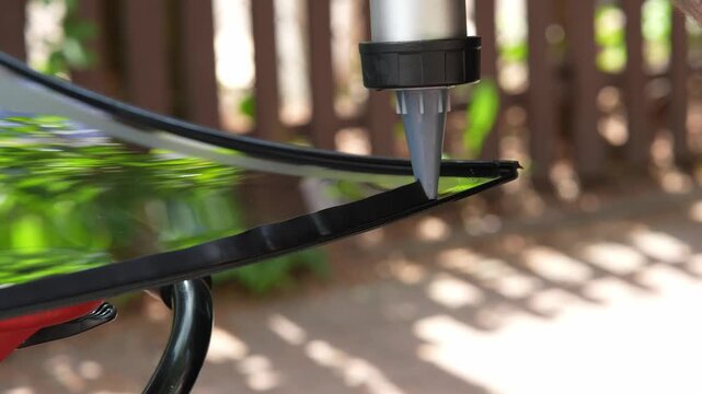 Auto glass installation applying sealant bead with a caulking gun in 4K. Worker hand dispensing polyurethane bonding adhesive onto the border of replacement glass before vehicle installation