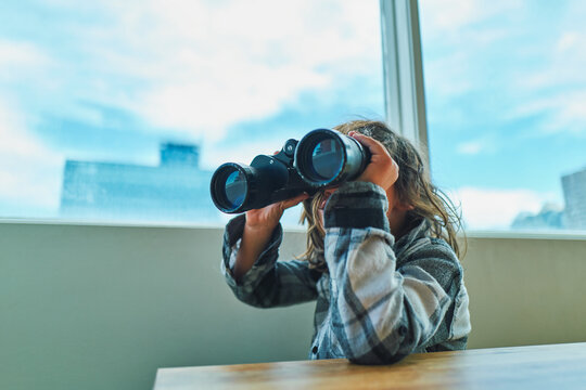 Curious boy scanning the city with binoculars from an apartment