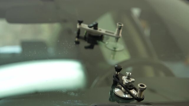 Hands using a syringe to load clear polymer adhesive into a metal injector bridge for professional chip repair. 4K stock video of vehicle window restoration