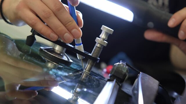 Technician using a metal probe to agitate the glass around an injector tool, forcing air bubbles out of the resin fill. 4K video of releasing air pockets during windshield resin injection