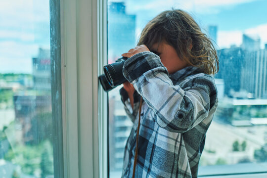 Boy looking through binoculars at the city from a high-rise window