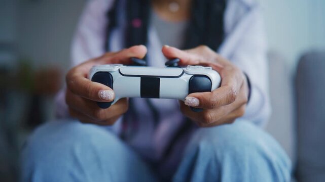 Person holds a white game controller while sitting on a couch in a living room during the evening