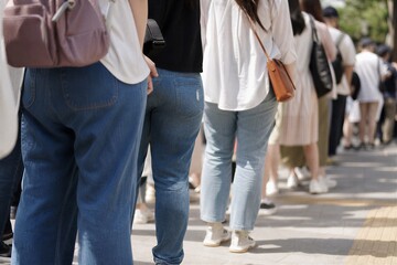 Fototapeta premium Pedestrians queuing on a bustling urban sidewalk during a summer festival, seen from behind.