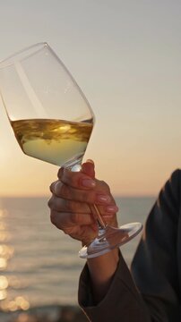 Hand holding wine glass against sunset over ocean background  