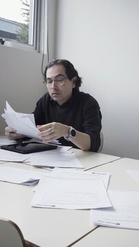 Vertical portrait of a tired male teacher taking off his glasses and rubbing his eyes in extreme fatigue at a desk