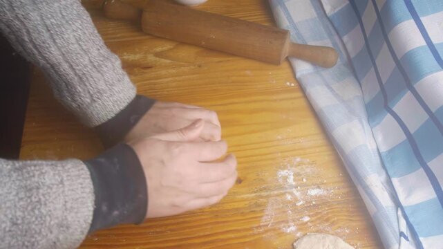 Top view of hands gathering and rolling out homemade dough with a rolling pin