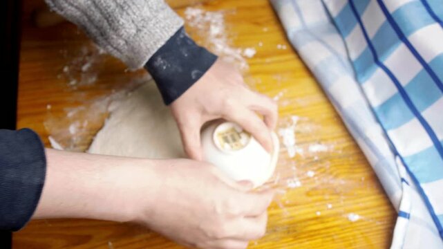 Top view of hands cutting round shapes from raw dough using a small bowl