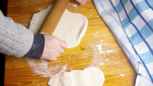 Top view of baker's hands flattening fresh pastry dough with a wooden rolling pin