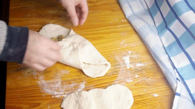 Top view of baker folding and sealing minced meat filling inside raw empanada dough