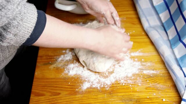 Top view of baker hands kneading raw dough on a floured wooden table