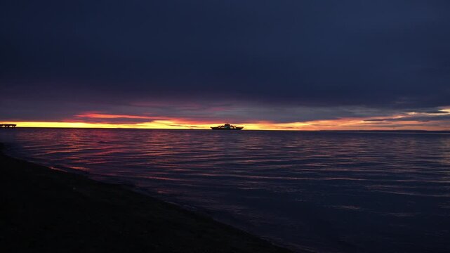 Silhouette of a passenger ferry boat sailing across the sea at sunset with dramatic colorful sky