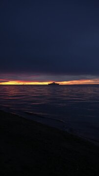 Vertical shot of passenger ferry boat silhouetted against dramatic sunset horizon