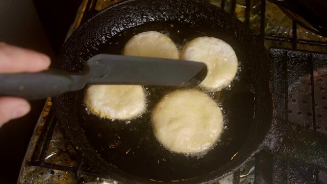 Top view of baker flipping traditional Chilean sopaipillas in a frying pan with boiling oil