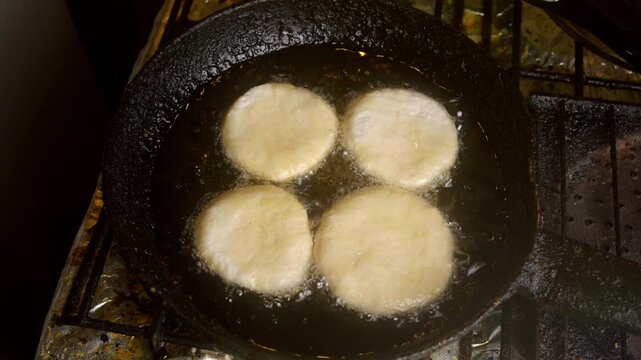 Top view of raw sopaipilla dough discs beginning to deep fry in hot oil