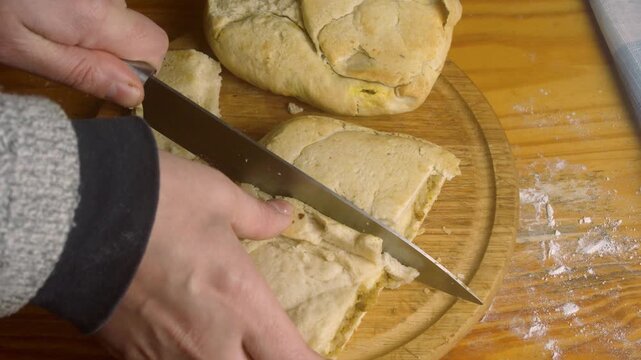 Close up of hands cutting homemade rustic bread filled with meat onto a wooden board