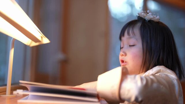 Soft light bathes a child reading quietly. Her eyes close in gentle focus, absorbed in the book. Warm glow creates a cozy, peaceful atmosphere. Ideal for scenes of quiet learning or bedtime routines
