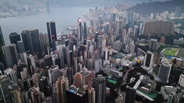 Midday kowloon financial district from drone point of view at day time. Crisp visibility highlights office towers and grid of streets and plazas. Aerial footage of harbor edge with busy vessels