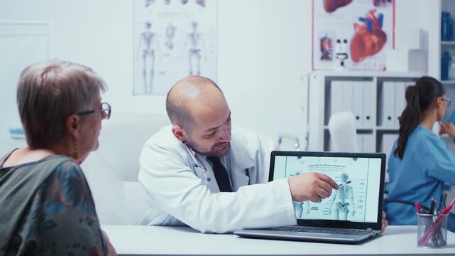 Young male doctor explains how an elderly retired woman can avoid bone problems, using radiology guidance in a modern private clinic.