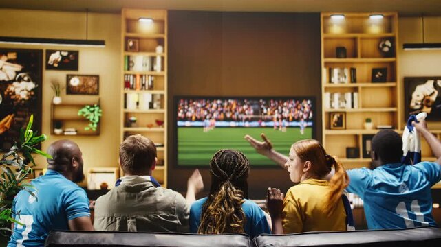 Joyous football supporters do a high five at home after a goal as thrilled soccer fans cheer during an apartment watch party after a team win.