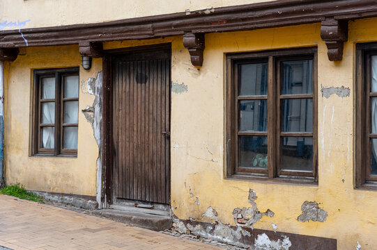 Weathered Historic House Facade with Peeling Plaster, Wooden Door and Traditional Windows