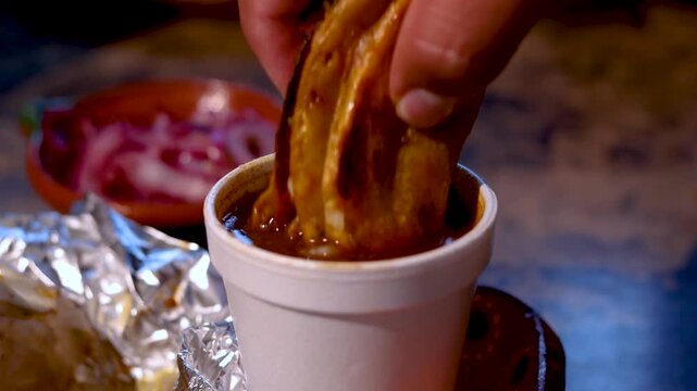 Delicious mexican birria taco being dipped into a rich and flavorful consomm&eacute; stew