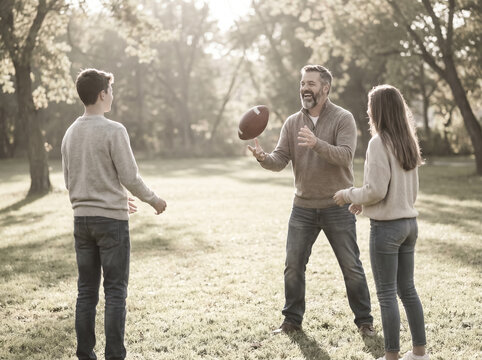 Smiling mature man throwing American football to his teen children