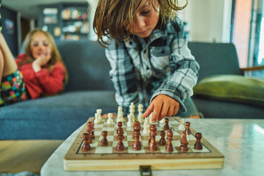 Boy making a chess move while his brother smiles behind him