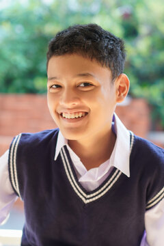 Smiling Asian school boy in uniform portrait with natural light and soft green background. Education, childhood, happiness, back to school concept.