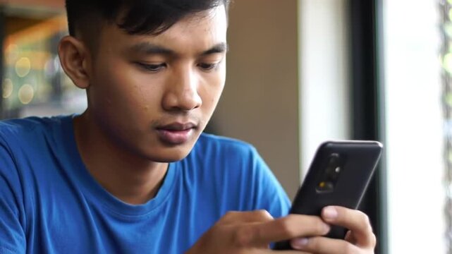 Young man in blue t-shirt using smartphone, close-up, casual, indoor setting