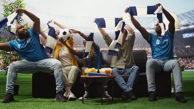 Football fans enjoy an immersive match at home with beer and team scarves, creating loud crowd energy and stadium atmosphere on the couch.