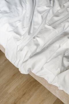 White unmade bed with rumpled sheets in a minimalist bedroom setting
