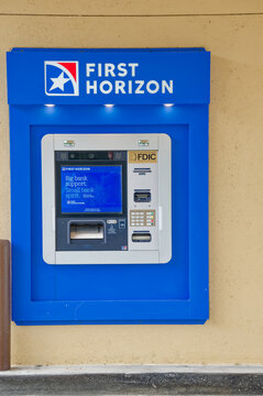 A First Horizon bank ATM mounted in a bright blue kiosk against a beige wall. Editorial Use Only July 11, 2026 St. Petersburg, FL USA showing FDIC signage, card reader, keypad and cash slot; clean ext