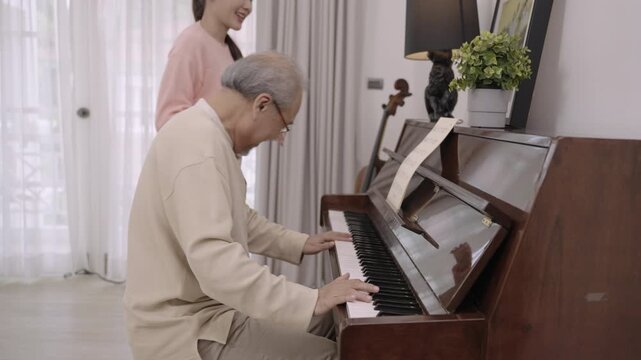 Happy Asian senior elderly father and his beautiful daughter sit playing piano and singing together having fun and enjoying in living room at home. Lifestyle and leisure after retirement with family. 