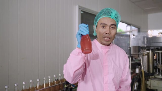 Professional Asian inspector in uniform of food and drink factory holding a juice beverage bottle promoting and advertising healthy nutritional benefits in production line at a manufacturing industry.