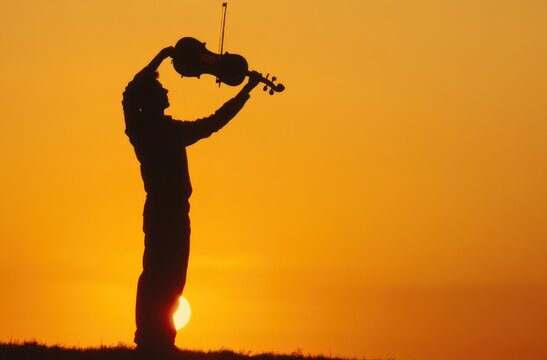 silhouette of person holding violin and bow overhead at sunset on grassy ridge, triumphant joyful pose