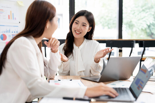 Two Young Asian Businesswomen Having Discussion and Gesturing at Office Desk