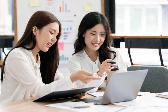 Two Smiling Asian Businesswomen Working Together on Laptop in Modern Office