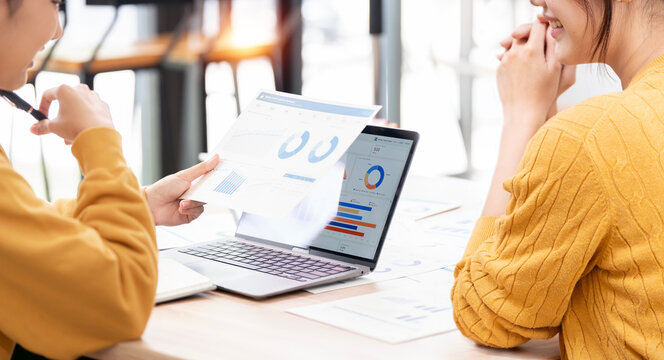 Businesswomen analyzing financial charts on laptop and paper in office.