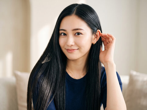 黒髪ストレートロングヘアの美しい髪を耳にかける笑顔の女性