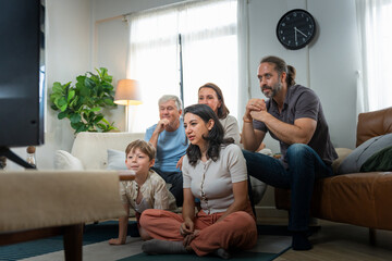 Fototapeta premium Multi-generational family watching television together in living room, Happy family sitting on the couch and floor watching movie at home, Family spending time together watching TV in cozy living room