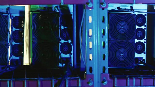 Bitcoin mining rigs with dual cooling fans and connected power and data cables on a metal shelf in a server room
