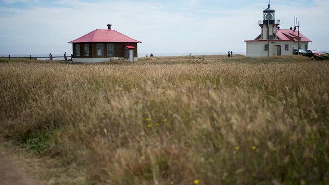 Visitors walk along trails near Point Cabrillo Lighthouse in Mendocino California on a sunny day by the Pacific Ocean.
