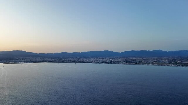Aerial view from a jet cockpit of Palma de Mallorca city and bay at sunset, flying over the mediterranean sea at low altitude, with a sining sun sinking beneath the Tramontana range.