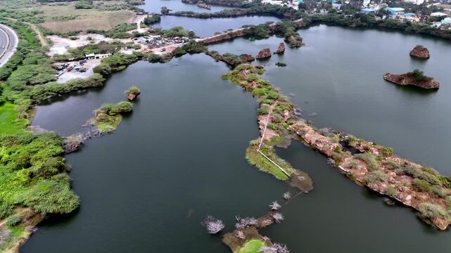 Cinematic aerial view of the Granite Quarry featuring flooded quarry lakes, rocky granite islands, lush wetlands, and the nearby Chennai Bypass, showcasing a dramatic post-mining landscape.