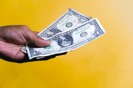 Close up of a person hand holding and giving US dollar banknotes isolated on yellow background. Financial, payment, or tipping concept.