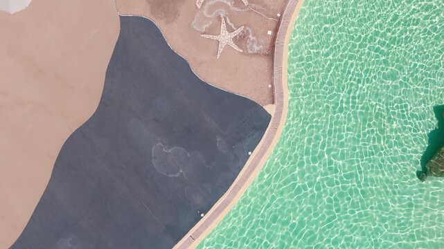 Top-down drone view of turquoise pool, mosaic starfish, and poolside textures