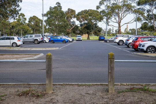 A pedestrian gap between timber bollards provides walking access to a suburban carpark bordered by public green space in Melbourne, Australia. Public infrastructure, pedestrian safety design