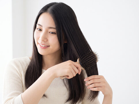 ヘアブラシで黒髪を梳かしてヘアケアをする笑顔の女性